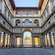 A courtyard featuring columns and arches with the Uffizi Gallery in Florence, Italy in the background